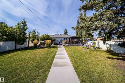 Expansive backyard featuring a central concrete pathway, a wooden deck with a screened enclosure, and mature trees - 10245 160 Street Nw, Edmonton, AB 