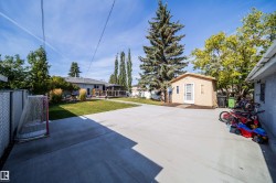 Expansive concrete patio with a detached shed, chain-link fence, and mature trees - 