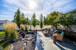 Concrete patio with mature trees, a rock-lined pond, and tall ornamental grasses - 