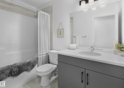 White tub with a tile surround, dark gray vanity with an integrated sink, polished chrome faucet, and a large wall-mounted mirror - 