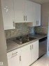 White high-gloss cabinetry, stainless steel double-basin sink, mosaic tile backsplash, stainless steel dishwasher, and tiled flooring - #503 11211 85 St Nw, Edmonton, AB 