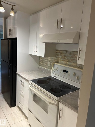 White flat-panel cabinetry, light-toned countertops, tiled backsplash, white electric range, and a black refrigerator - #503 11211 85 St Nw, Edmonton, AB 