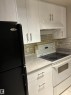 White upper cabinetry with brushed nickel hardware, white range hood, light-toned backsplash, white base cabinetry with brushed nickel hardware, and a black refrigerator - #503 11211 85 St Nw, Edmonton, AB 