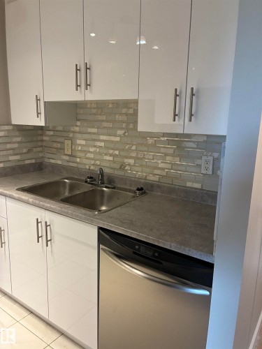 White high-gloss cabinetry with bar pull hardware, mosaic tile backsplash, dual basin stainless steel sink, and stainless steel dishwasher - #503 11211 85 St Nw, Edmonton, AB 