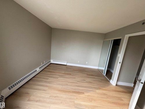 Wood-finish flooring with a neutral wall color, mirrored closet doors, and white trim - #503 11211 85 St Nw, Edmonton, AB 