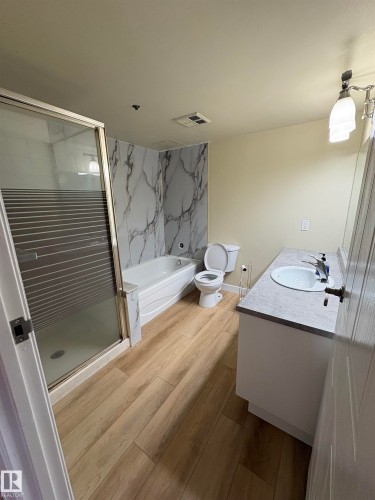 Wood-finish flooring with a glass-enclosed shower, built-in bathtub, and a vanity with a drop-in sink - #503 11211 85 St Nw, Edmonton, AB 