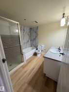 Wood-finish flooring with a glass-enclosed shower, built-in bathtub, and a vanity with a drop-in sink - 