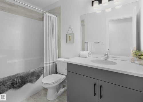 White tub with a tile surround, dark gray vanity with an integrated sink, polished chrome faucet, and a large wall-mounted mirror - 129 Chelles Wynd, St. Albert, AB 