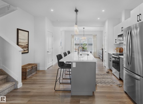 Contemporary kitchen featuring a large island with sink, stainless steel appliances, white cabinetry, and wood-finish flooring - 129 Chelles Wynd, St. Albert, AB 