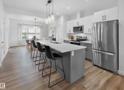 Kitchen featuring a large island with seating, stainless steel appliances, two-tone cabinetry, white subway tile backsplash, and wood-finish flooring - 