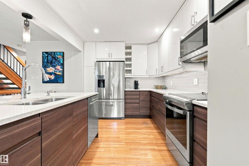 Modern kitchen featuring two-tone cabinetry, stainless steel appliances, light countertops, a subway tile backsplash, and wood-finish flooring - 141 Hearthstone Nw, Edmonton, AB - Indoor Photo Showing Kitchen With Double Sink