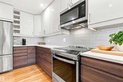 Modern kitchen featuring two-tone cabinetry, stainless steel appliances, light gray subway tile backsplash, white countertops, and hardwood flooring - 