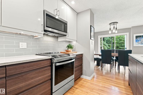 Modern kitchen featuring two-tone cabinetry, a stainless steel range with an over-the-range microwave, light-toned countertops, and a subway tile backsplash - 141 Hearthstone Nw, Edmonton, AB - Indoor Photo Showing Kitchen With Upgraded Kitchen
