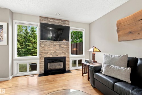 Living area featuring a stone veneer fireplace with a black hearth, light wood-finish flooring, and multiple windows - 141 Hearthstone Nw, Edmonton, AB - Indoor Photo Showing Living Room With Fireplace