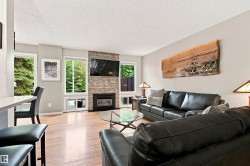 Living area featuring wood-finish flooring, a stacked stone fireplace surround, multiple windows, and a built-in hearth - 