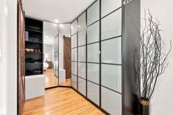 Corner closet system featuring frosted glass panels with dark framing, integrated full-length mirrors, and rich wood-finish flooring - 