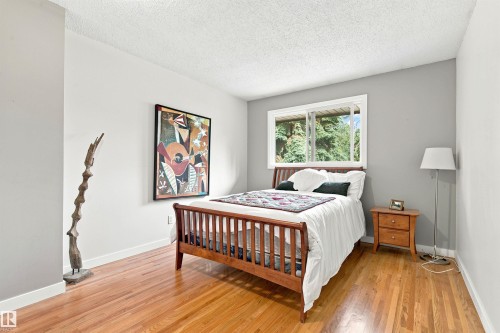 Spacious room featuring wood-finish flooring, a large window with exterior foliage, and light gray walls - 141 Hearthstone Nw, Edmonton, AB - Indoor Photo Showing Bedroom