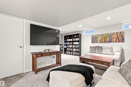 Recreation room featuring recessed lighting, two transom windows, light-colored carpeting, a built-in shelving unit, and a mounted television - 141 Hearthstone Nw, Edmonton, AB - Indoor