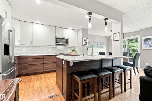 Kitchen featuring a central island with countertop seating, stainless steel appliances, wood-finish flooring, white subway tile backsplash, and sliding glass doors - 141 Hearthstone Nw, Edmonton, AB - Indoor Photo Showing Kitchen With Upgraded Kitchen