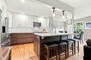 Kitchen featuring a central island with countertop seating, stainless steel appliances, wood-finish flooring, white subway tile backsplash, and sliding glass doors - 141 Hearthstone Nw, Edmonton, AB  - Indoor Photo Showing Kitchen With Upgraded Kitchen 
