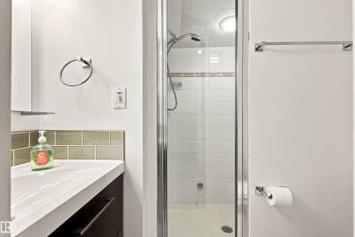 Compact bathroom featuring a glass-enclosed shower with white subway tile, a white vanity with integrated sink, and an accent tile backsplash - 141 Hearthstone Nw, Edmonton, AB - Indoor Photo Showing Bathroom