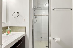 Compact bathroom featuring a glass-enclosed shower with white subway tile, a white vanity with integrated sink, and an accent tile backsplash - 