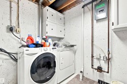 Dedicated laundry area featuring white shaker-style wall cabinets and exposed utility pipes - 