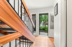 Entryway featuring wood-finish flooring, a contemporary staircase with wood and black metal railings, and a glass-paneled entry door - 