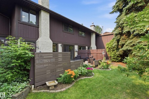 Private patio area with a wooden privacy screen, adjacent to a manicured lawn and mature landscaping - 141 Hearthstone Nw, Edmonton, AB - Outdoor With Exterior