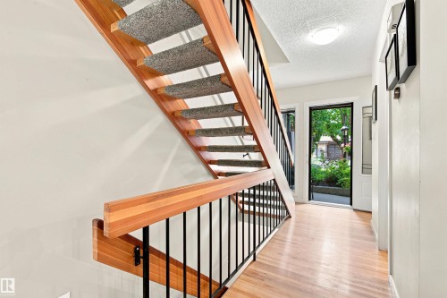 Hardwood-style flooring extends from the entryway, featuring an open staircase with wood railings and black metal spindles - 141 Hearthstone Nw, Edmonton, AB - Indoor Photo Showing Other Room