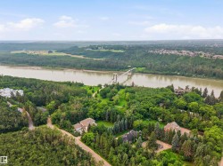 Aerial perspective showcasing a broad river, extensive natural landscapes, a suspension bridge, and residential properties nestled among dense trees - 
