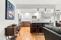 Open-concept kitchen featuring wood-finish flooring, two-tone cabinetry, stainless steel appliances, a white subway tile backsplash, and a central island with integrated seating - 
