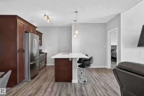 Kitchen featuring wood-finish flooring, dark wood cabinetry, stainless steel appliances, and a central island with a white countertop - #411 304 Ambleside Link Li Sw, Edmonton, AB 