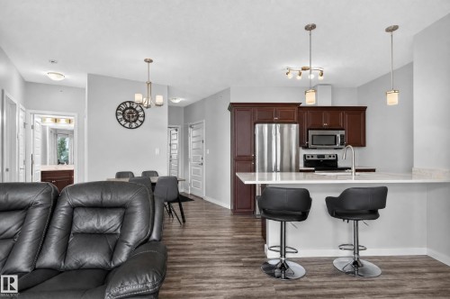 Kitchen with dark wood cabinetry, stainless steel appliances, and a light-toned countertop with breakfast bar seating - #411 304 Ambleside Link Li Sw, Edmonton, AB 