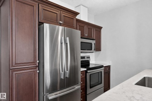 Stainless steel appliance package, dark wood cabinetry with crown molding, light-colored countertops, undermount sink, and recessed lighting - #411 304 Ambleside Link Li Sw, Edmonton, AB 