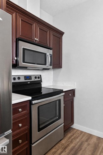 Rich wood-finish cabinetry, stainless steel appliances, white countertops, and wood-finish flooring - #411 304 Ambleside Link Li Sw, Edmonton, AB 