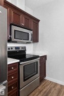 Rich wood-finish cabinetry, stainless steel appliances, white countertops, and wood-finish flooring - 