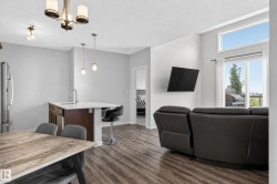 Open-concept living space featuring wood-finish flooring, a kitchen island with seating, stainless steel refrigerator, and large windows with a transom - 