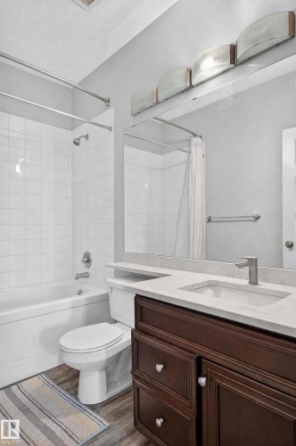 Dark wood-finish vanity with drawer and cabinet storage, light-toned countertop, undermount sink with a brushed nickel faucet, and a tiled shower-tub combination - #411 304 Ambleside Link Li Sw, Edmonton, AB 