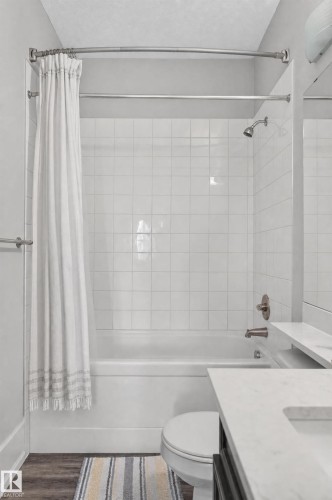 Bathtub with white square tile surround, brushed nickel fixtures, and wood-finish flooring - #411 304 Ambleside Link Li Sw, Edmonton, AB 
