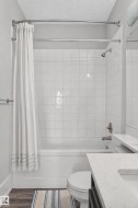 Bathtub with white square tile surround, brushed nickel fixtures, and wood-finish flooring - 