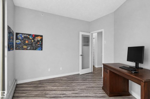 Wood-finish flooring, light gray wall paint, white trim, and a partially open door with frosted glass paneling - #411 304 Ambleside Link Li Sw, Edmonton, AB 