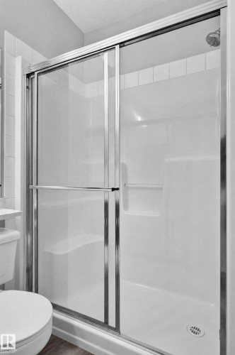 White shower stall with a built-in shelf, chrome shower head, and sliding glass doors with chrome framing - #411 304 Ambleside Link Li Sw, Edmonton, AB 