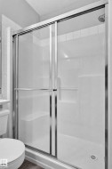 White shower stall with a built-in shelf, chrome shower head, and sliding glass doors with chrome framing - 