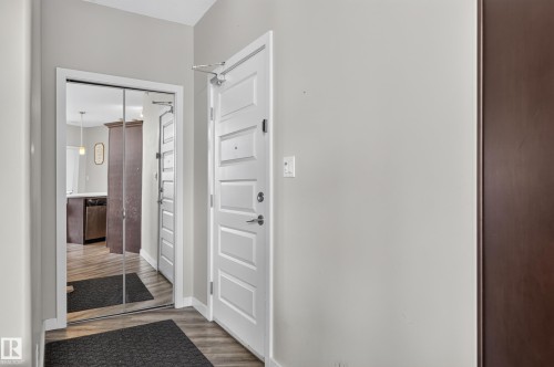 Entryway featuring wood-finish flooring, white paneled doors, and full-length mirrored closet doors - #411 304 Ambleside Link Li Sw, Edmonton, AB 