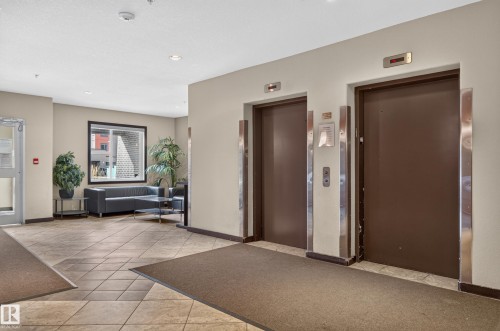 Elevator access featuring two units with stainless steel accents, tile flooring, and a large window - #411 304 Ambleside Link Li Sw, Edmonton, AB 
