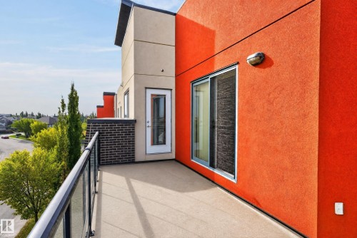 Private balcony featuring a glass and metal railing, textured stucco exterior, and sliding glass door access - #411 304 Ambleside Link Li Sw, Edmonton, AB 