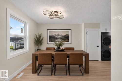 Spacious dining area featuring wood-finish flooring, a large window, a modern ceiling light fixture, and a built-in stacked laundry unit - 13511 114 Street Nw, Edmonton, AB 