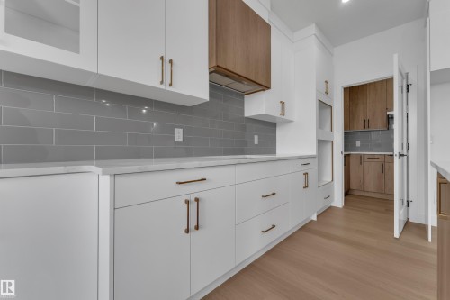 White flat-panel cabinetry with bronze hardware, gray subway tile backsplash, light-toned wood-finish flooring, and white countertops - 4212 63 Street, Beaumont, AB 