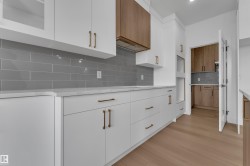 White flat-panel cabinetry with bronze hardware, gray subway tile backsplash, light-toned wood-finish flooring, and white countertops - 